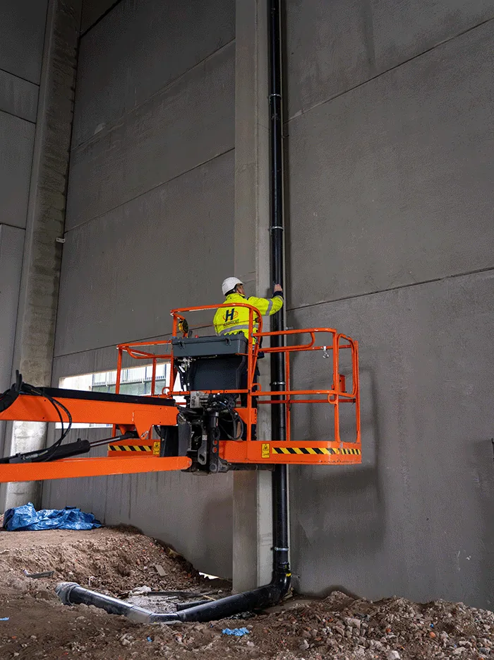 Een monteur van Hebbrecht op een hoogwerker plaatst een regenwaterafvoer in een grote hal